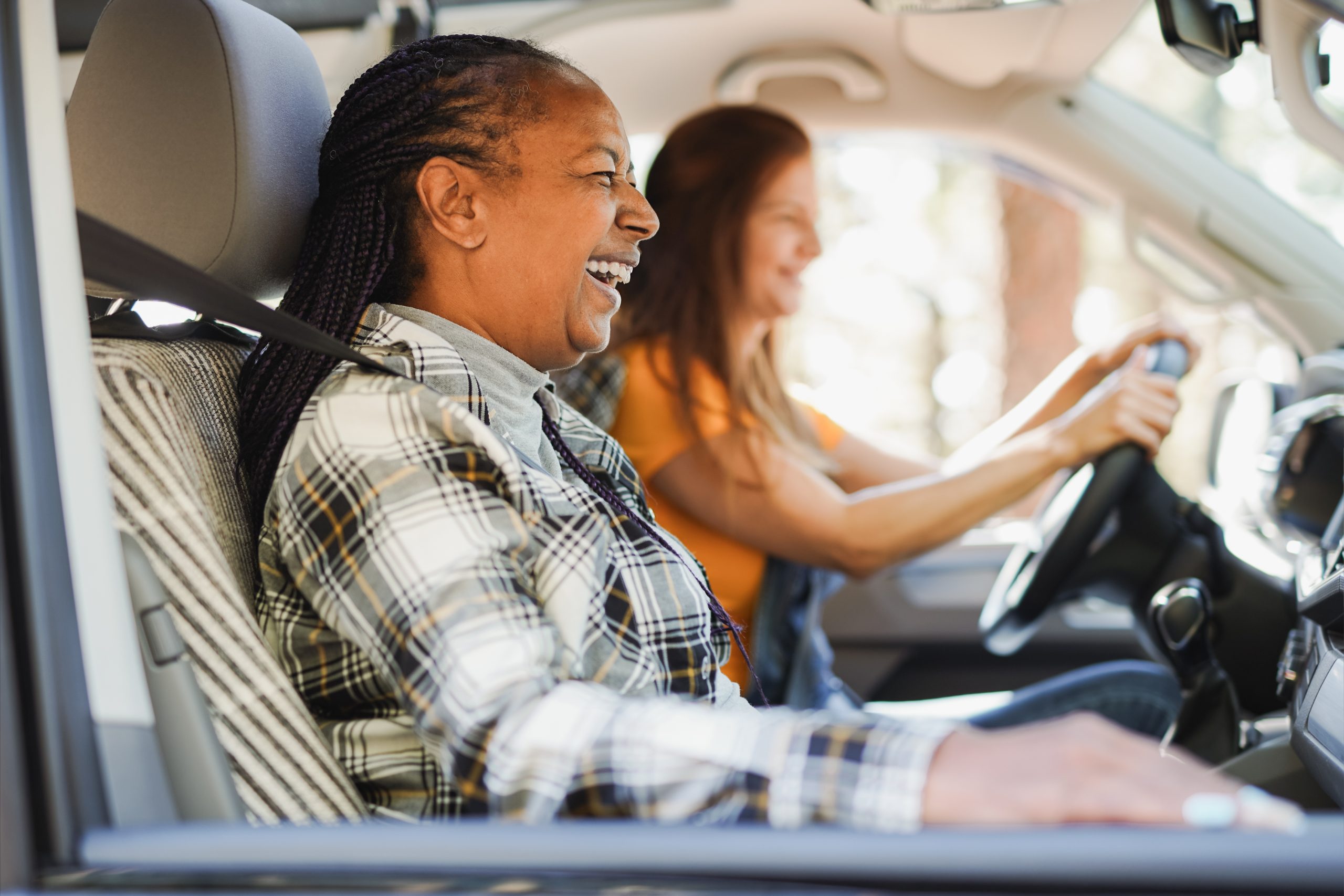 two women in a car. One is driving. The other is the passenger. They are both laughing while talking.