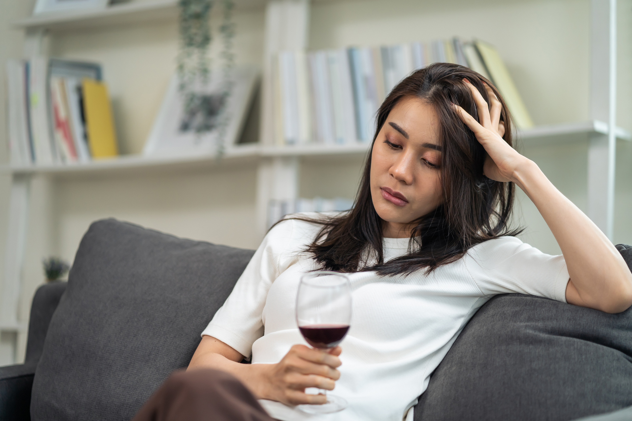 A young woman drinking a glass of wine looking sad.