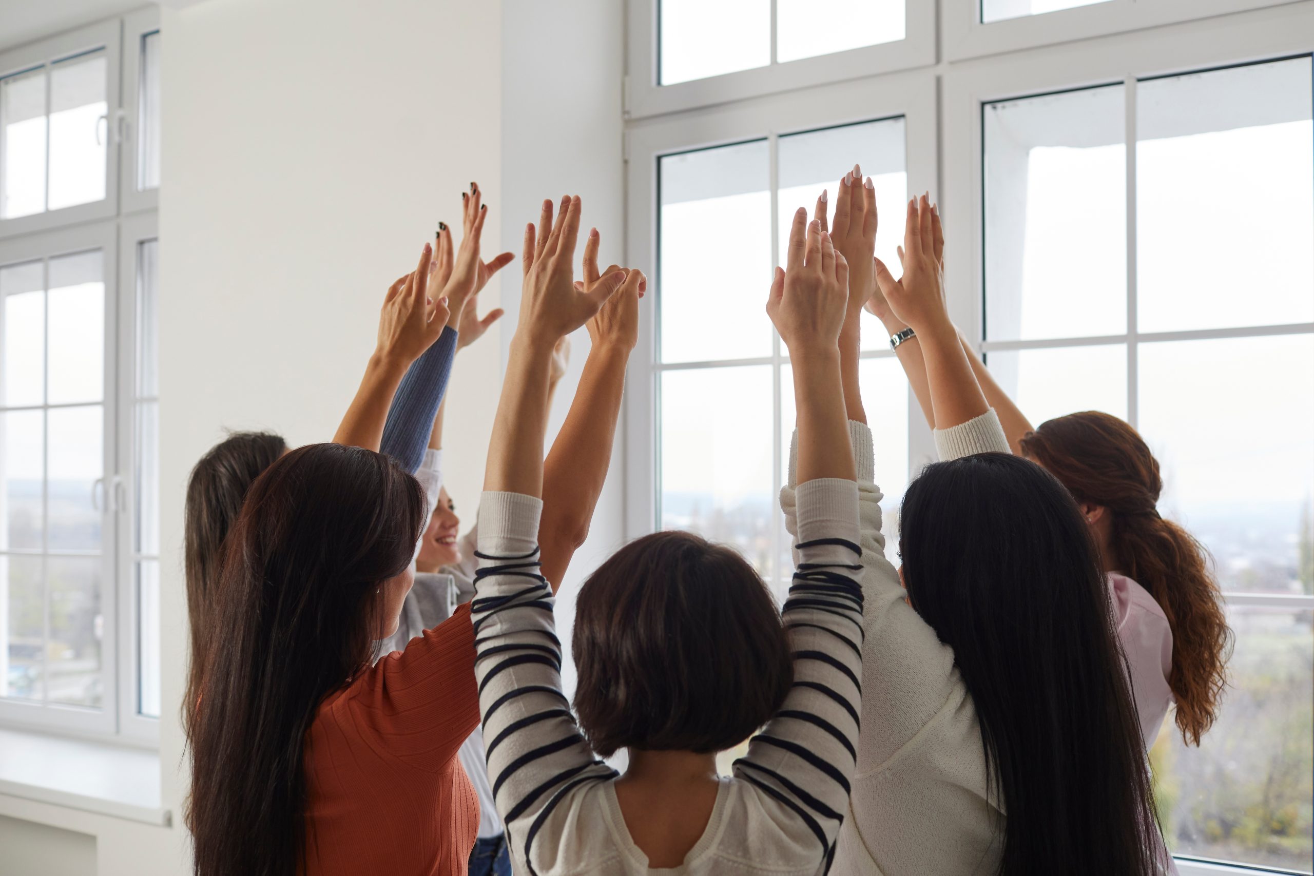 A diverse group of women in group therapy for depression. The women are standing in a circle with their arms raised celebrating their success and achievements.