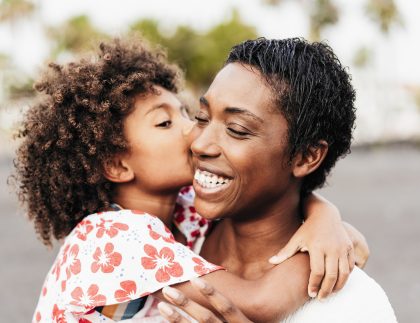 Happy woman with her daughter. The daughter is kissing her mom's cheek. The mom is laughing.