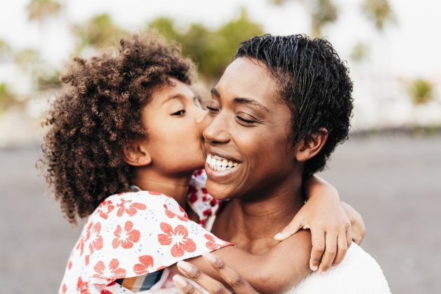 Happy woman with her daughter. The daughter is kissing her mom's cheek. The mom is laughing.