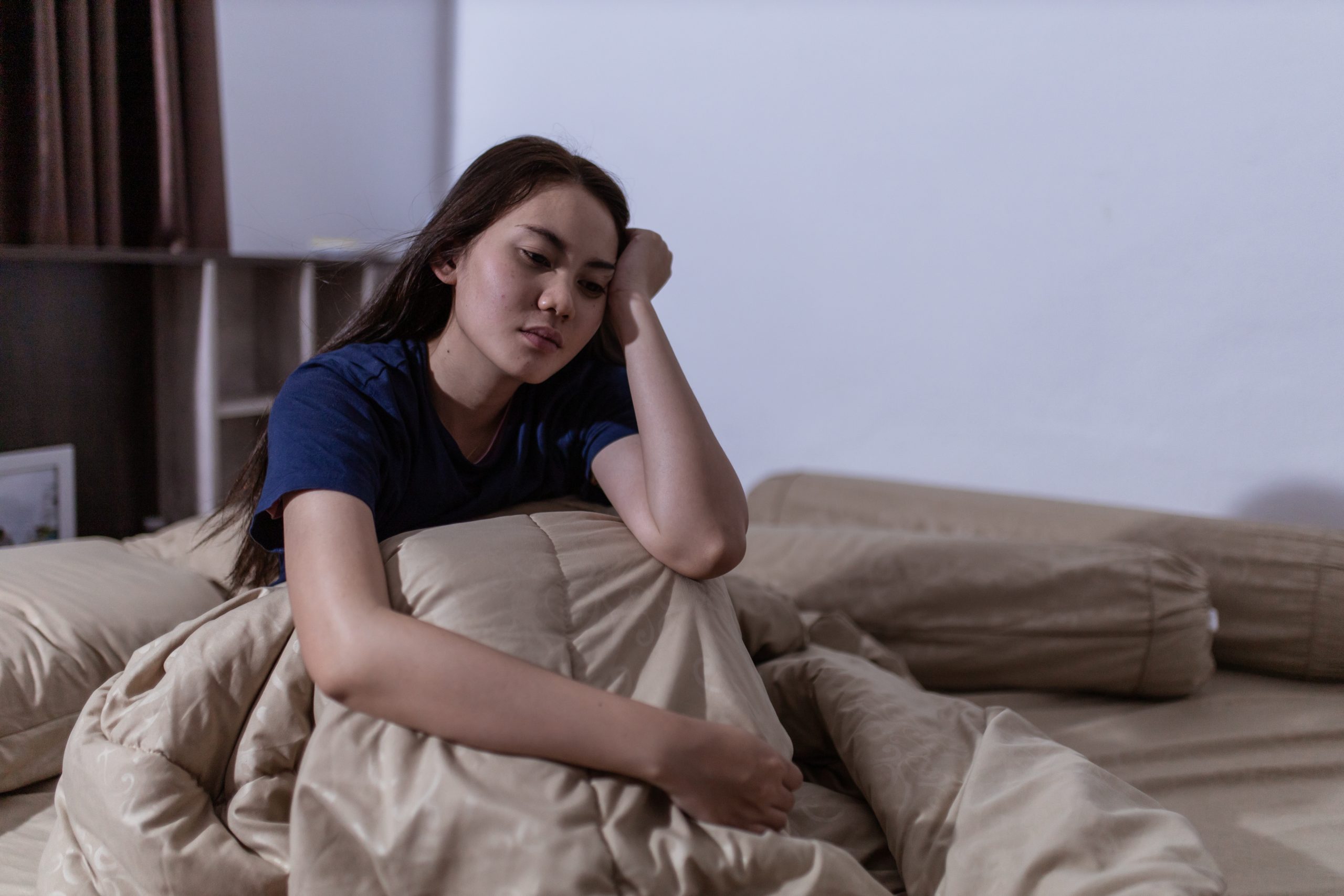 how sleep affects mental health; a young Asian woman struggling to sleep. She is lying awake in her bed with her hand over her head.