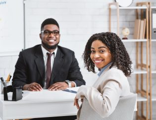 Career planning in recovery, represented by a young black woman interviewing for a new job. She is sitting at a desk being interviewed by the hiring manager, a black man in a suit.