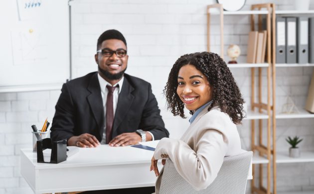Career planning in recovery, represented by a young black woman interviewing for a new job. She is sitting at a desk being interviewed by the hiring manager, a black man in a suit.