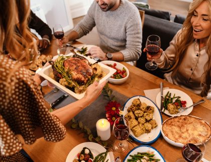 family and friends gathered around the dinner table about to eat Thanksgiving dinner. This image is a representation of managing stress around the holidays.