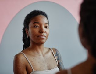 body image and addiction recovery; young black woman looking in a mirror, smiling