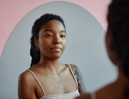 body image and addiction recovery; young black woman looking in a mirror, smiling