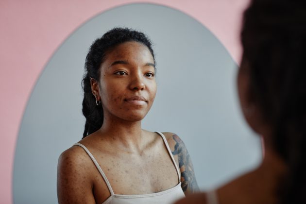 body image and addiction recovery; young black woman looking in a mirror, smiling